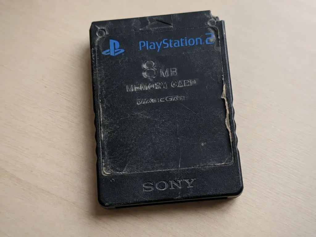 Close-up of a scratched black PlayStation 2 memory card with a chipped corner and peeling worn label.