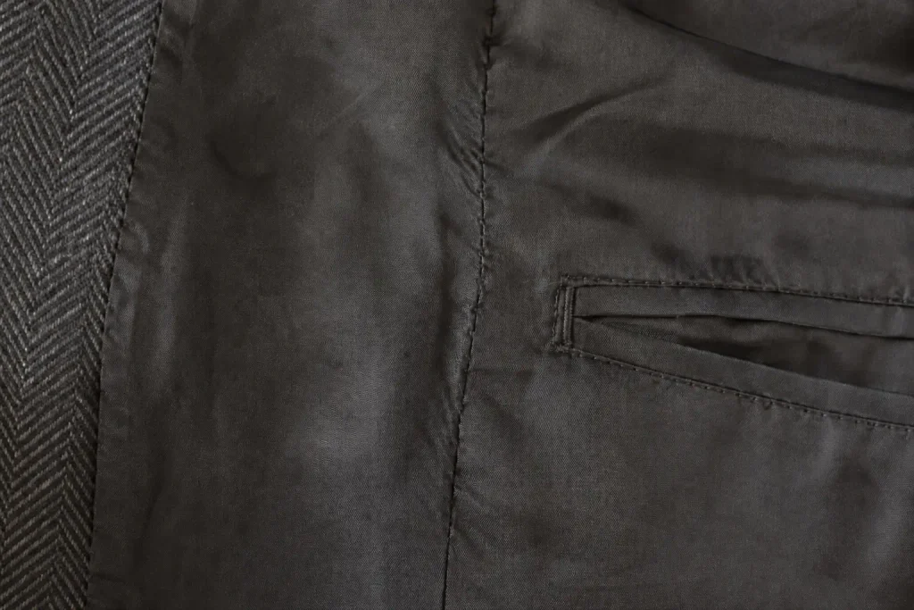 Close-up of a dark coat lining showing the stitched centre seam and an interior pocket.