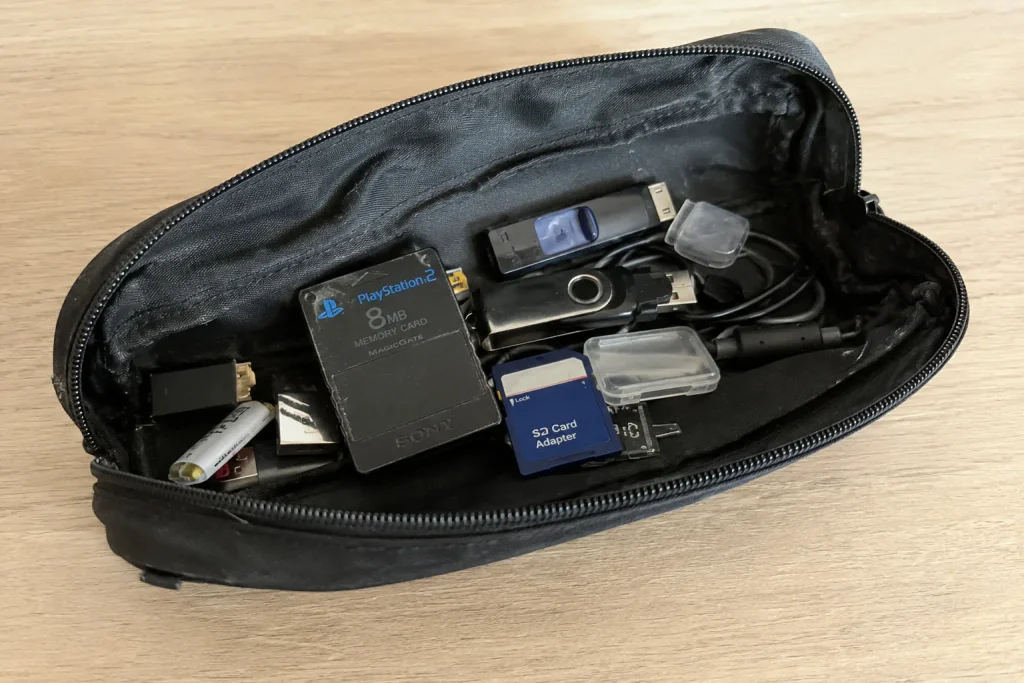 Open black pencil case containing a PlayStation 2 memory card, USB sticks, an SD-card adapter and small electronic odds and ends.