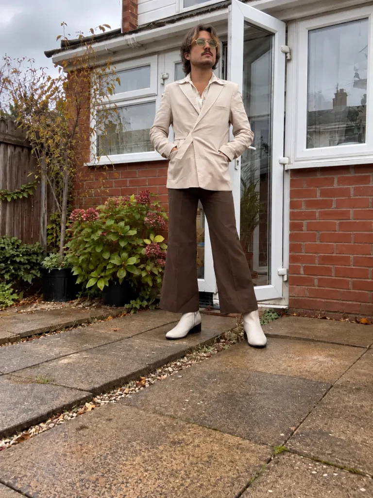 Cream jacket over a patterned vintage blouse, chocolate-brown flared trousers and white heeled ankle boots.