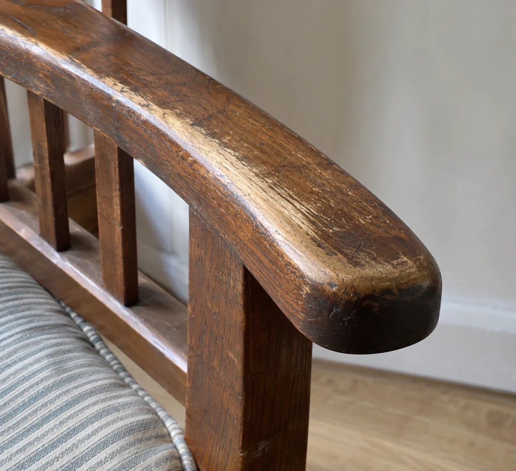 Wear concentrated along the top and outer edge of a wooden chair arm from repeated use.