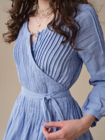 Close-up of a blue Linennaive wrap dress showing narrow pintucks across the bodice and a self-tie waist.
