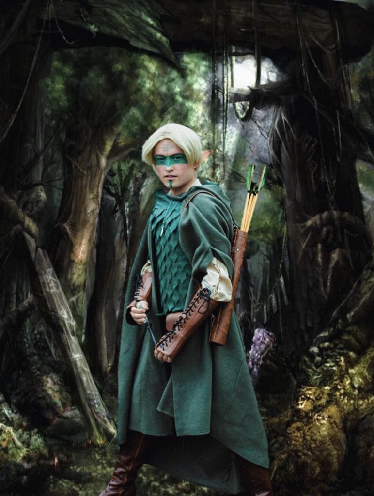 Olive green hooded wool cape with arm openings, worn in a woodland setting.