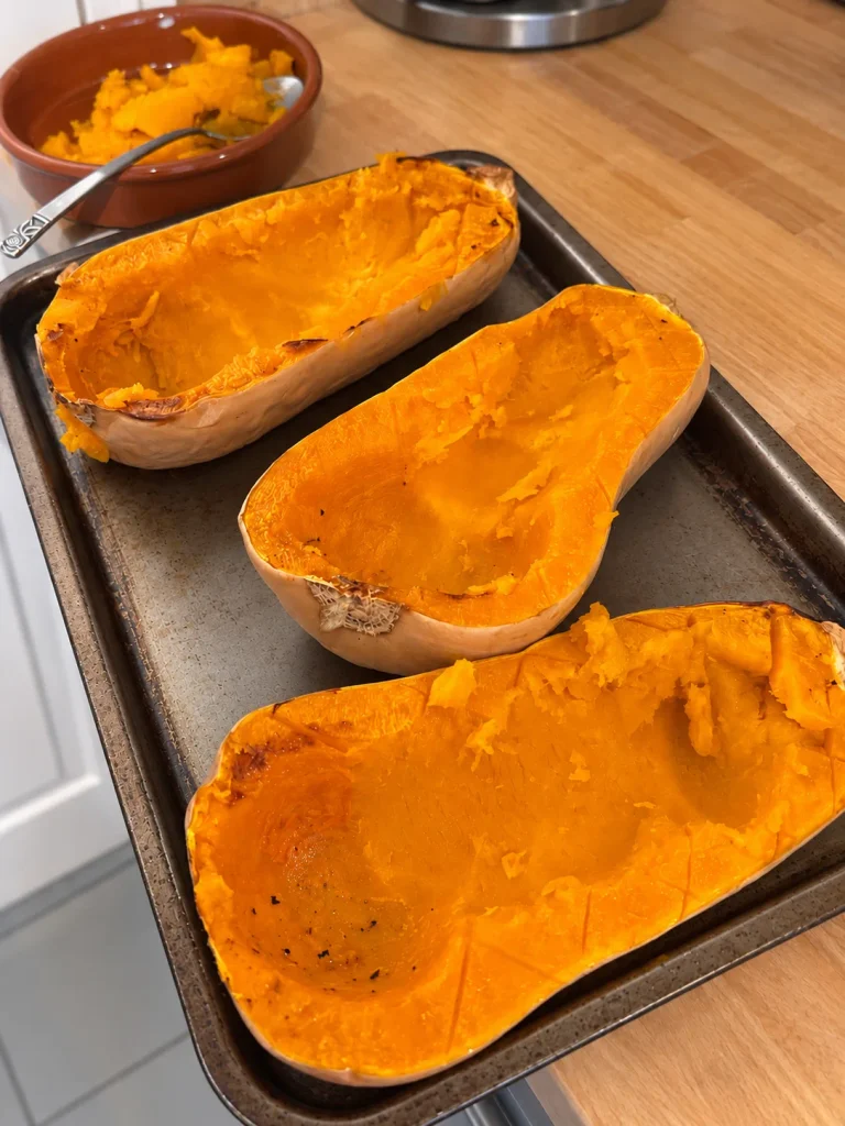 Three roasted butternut squash halves with the necks scooped into long troughs ready for stuffing.