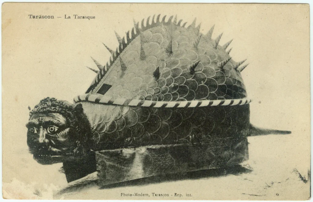 Early twentieth-century postcard showing the large spiked Tarasque processional effigy of Tarascon, with its broad shell-like body, carved face and long tail.