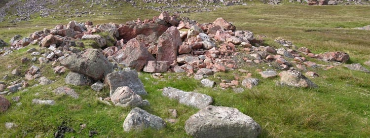 Ruined stone cairn known as Trowie Knowe in Shetland, set into a grassy landscape beside the road to North Roe.