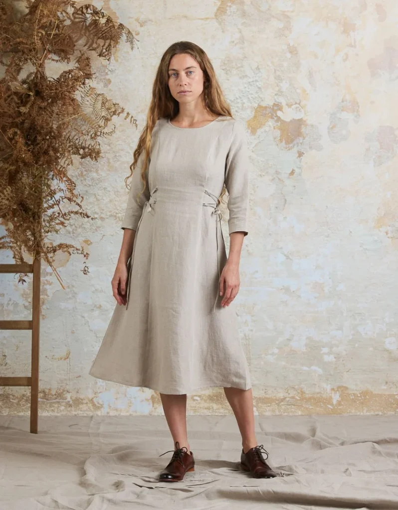 Woman wearing Voriagh’s Elina natural linen midi dress with a fitted bodice, three-quarter sleeves and adjustable side ties.