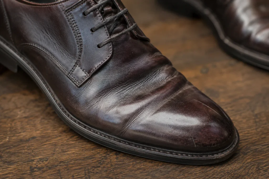 Close-up of a worn dark-brown leather shoe showing established creases across the forepart.