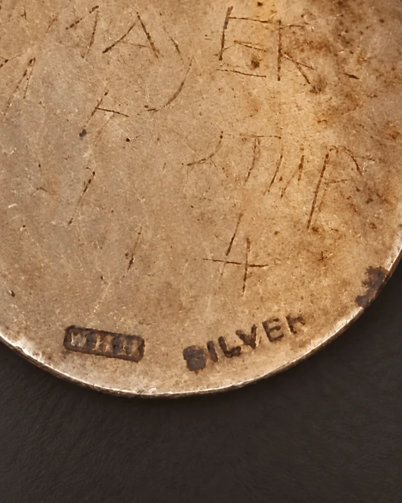 Close-up of the word SILVER and an unidentified rectangular punch on the back of a worn fob medal.