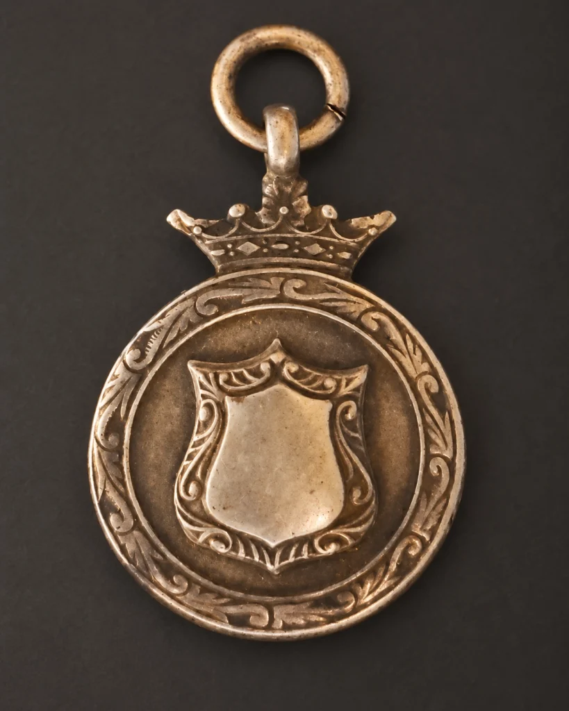 Front of a worn second-hand fob medal with a crown and blank central shield.