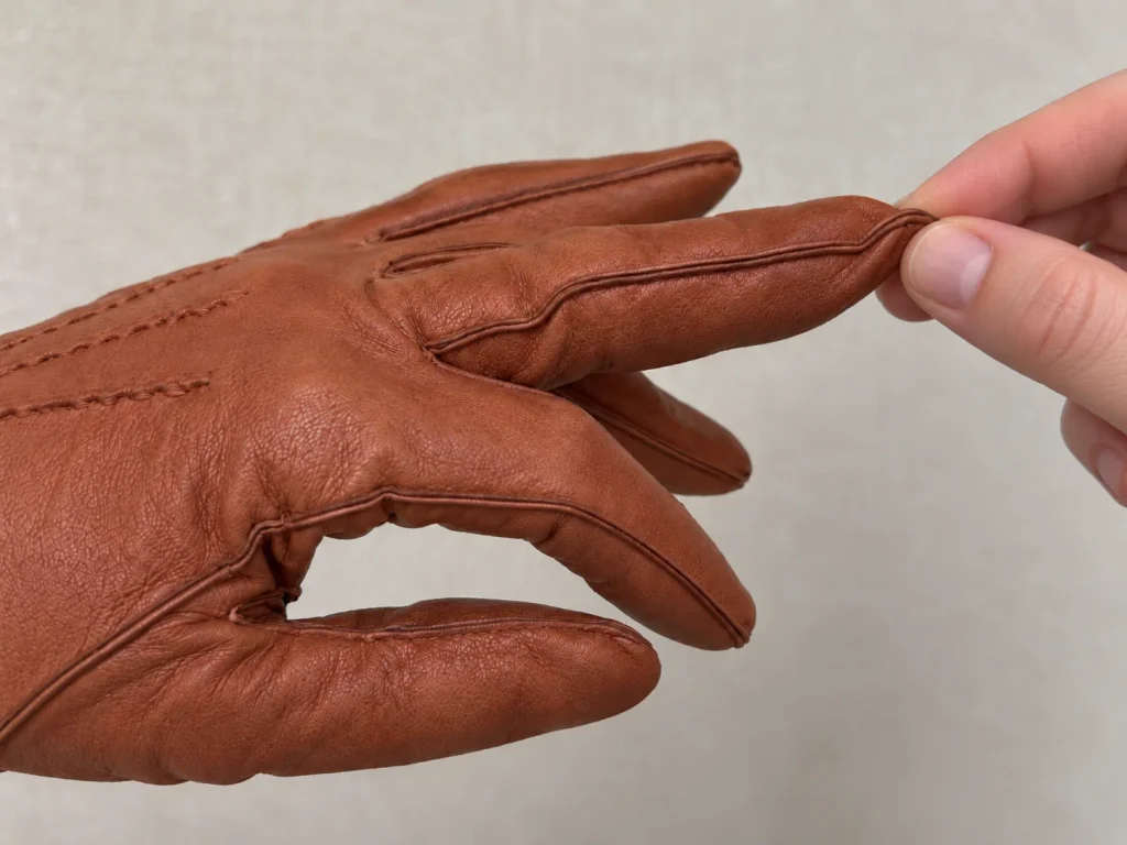 Gloved finger pinched beyond the wearer's fingertip to show excess length in the glove