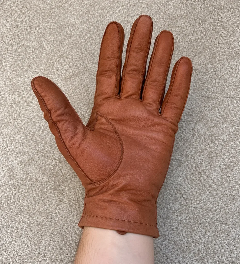 Palm of an oversized brown leather glove worn on a hand, showing spare material and creasing