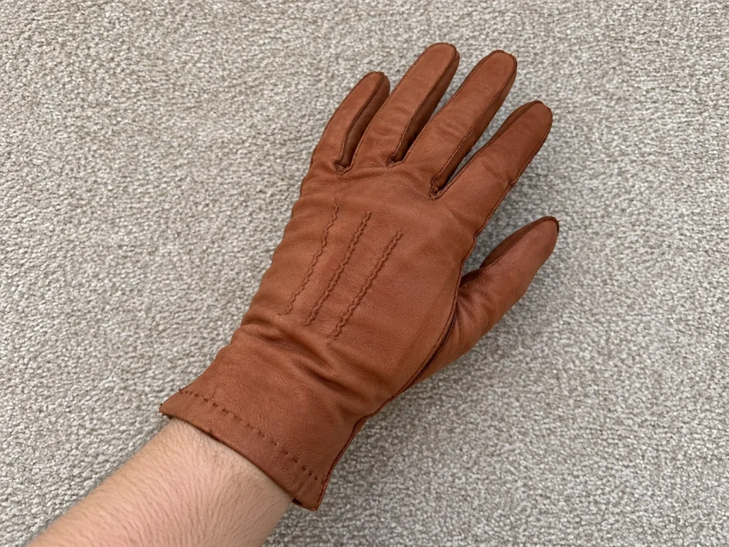 Brown leather glove worn on a hand with three wavy stitched points on the back